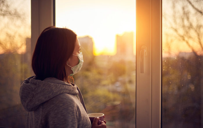 Woman near window at sunset in isolation at home for virus outbreak. Stay home concept