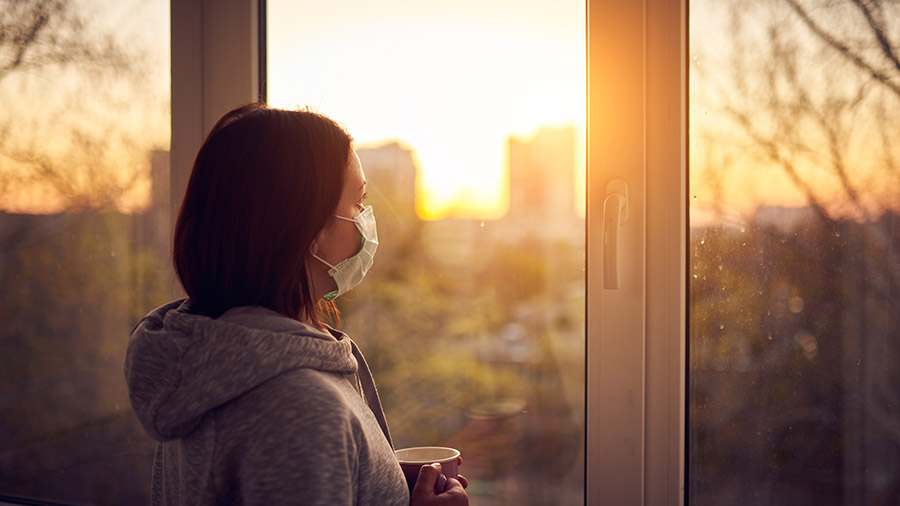 Woman near window at sunset in isolation at home for virus outbreak. Stay home concept